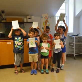 Campers showing off their science book sketches of marigold, or الآذريون نبات in Arabic.